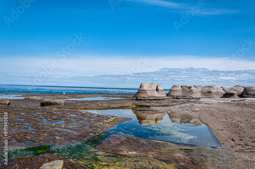 Sculptural formations etch the horizon at Île Nue de Mingan, where wind-swept monoliths stand sentinel over tranquil tidal pools under a serene sky. photo