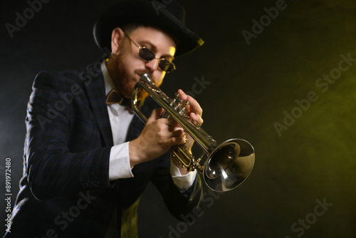 Professional musician playing trumpet on black background in color lights and smoke. Space for text