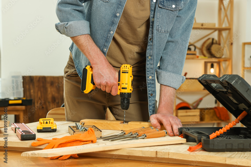 Craftsman working with drill at wooden table in workshop, closeup Craftsman working with drill at wooden table in workshop, closeup