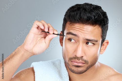 Man, thinking and tweezers by eyebrow in studio for grooming, facial epilation and wellness or skincare. Male person, cosmetic tool and product for hair removal, gray background and hygiene routine.