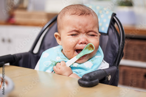 Baby, sad and crying or eating in home with spoon for nutrition, healthy development or tired in feeding chair. Child, unhappy or frustrated for reflux, problem and hungry in dining room of house