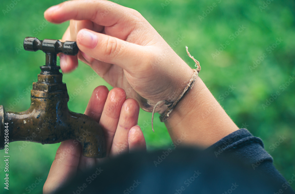 Φωτογραφία The hand of a child turning on water from a faucet that had no water during a shortage in order to drink