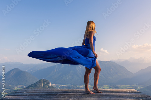 Woman in blue dress standing on wood platform with flying skirt above Austria alps. Loser panoramastrasse area photo