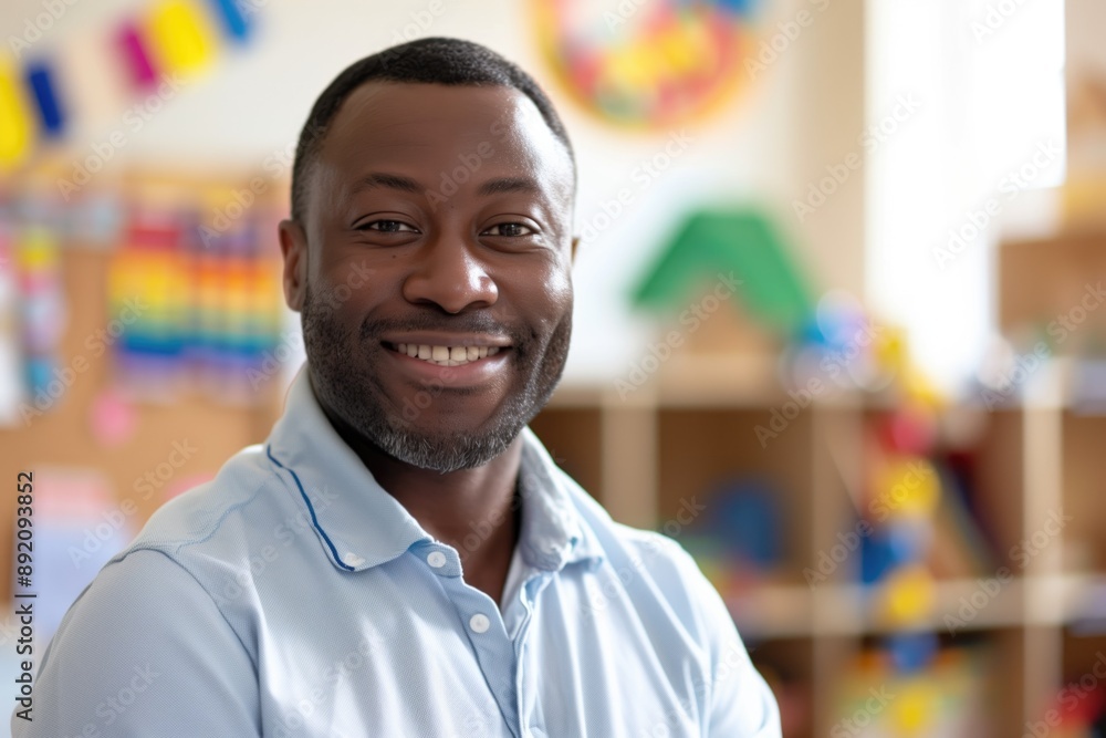 Smiling male teacher in light blue shirt with colorful kindergarten classroom background and educational toys.Educational setting, early childhood education, positive learning environment. Smiling male teacher in light blue shirt with colorful kindergarten classroom background and educational toys.Educational setting, early childhood education, positive learning environment.