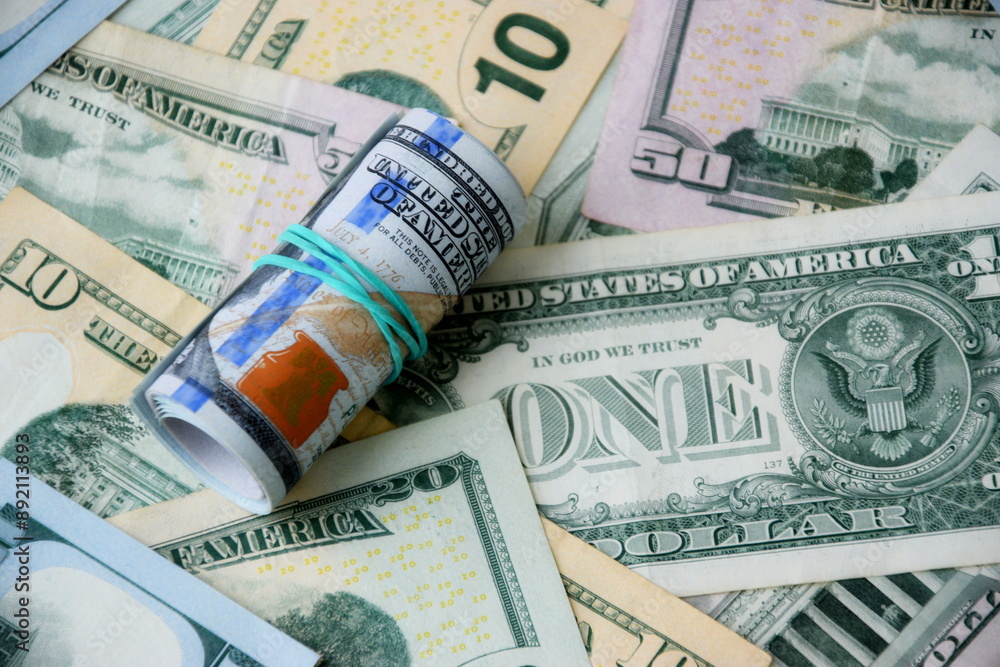 Hundred dollar bills roll lies on big amount of US dollars in different nominations under natural light Hundred dollar bills roll lies on big amount of US dollars in different nominations under natural light