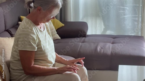 Close up of sad pensive 70s retiree woman put chin on folded palms experiences sentimental longing for period in past looks into distance, sit indoor. Melancholy, retired life, nostalgic mood concept