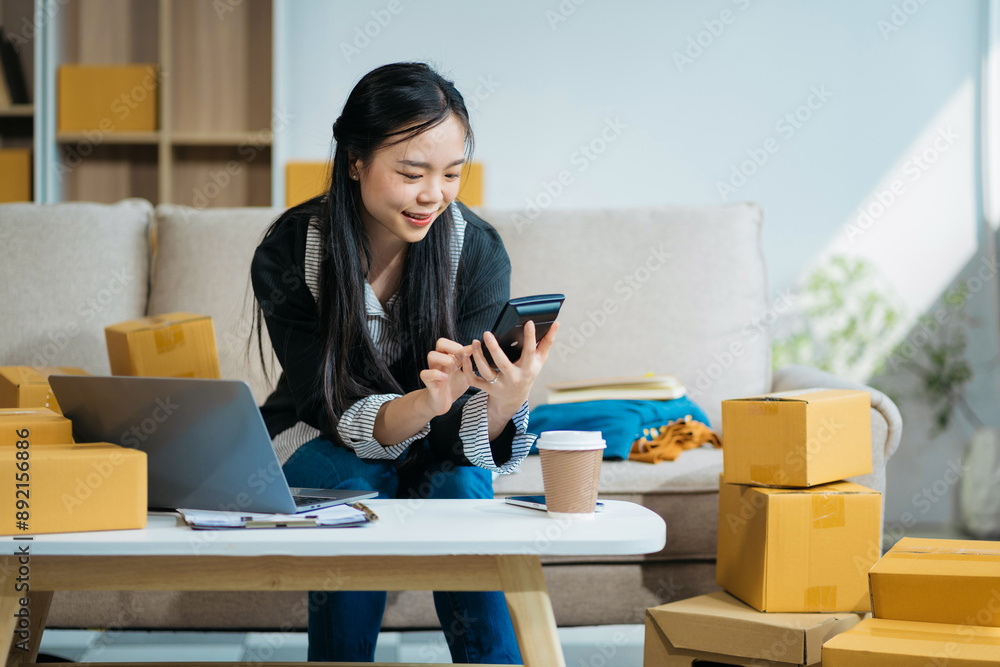 Entrepreneur using calculator in her hand, calculating financial expense at home office, online market packing box delivery,Startup successful small business owner, SME, concept. Entrepreneur using calculator in her hand, calculating financial expense at home office, online market packing box delivery,Startup successful small business owner, SME, concept.