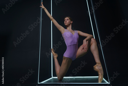 ballerina in a photo studio on a black background in a light led cube shows ballet elements and stretching photo