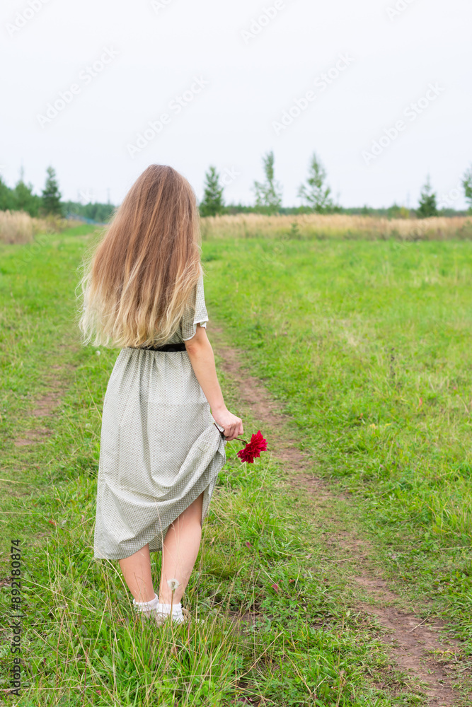 Φωτογραφία Blonde long haired young woman with red blooming dahlia flower in hand stand on road with green grass