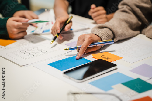 Wallpaper Mural Close-up of hands working on UX/UI design at a desk. Papers with wireframes, prototypes, and mockups detail user flows, personas, and A/B testing, ensuring usability and responsive design. Torontodigital.ca