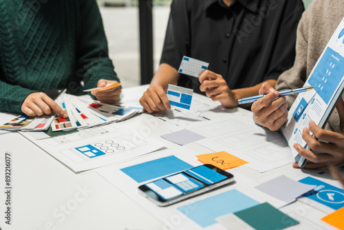 A group of people collaborates around a desk, discussing and reviewing user interface (UI) and user experience (UX) elements. usability, accessibility, and design principles for product development. photo