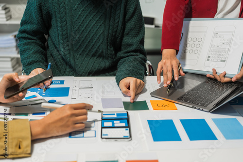 A group of people collaborates around a desk, discussing and reviewing user interface (UI) and user experience (UX) elements. usability, accessibility, and design principles for product development. photo