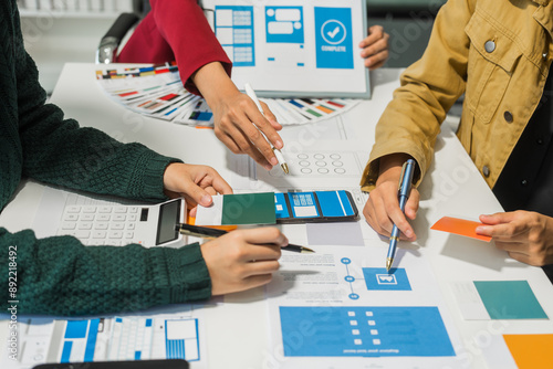 A group of people collaborates around a desk, discussing and reviewing user interface (UI) and user experience (UX) elements. usability, accessibility, and design principles for product development. photo