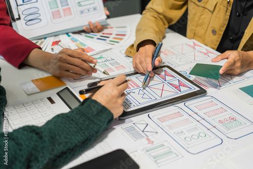 A group of people collaborates around a desk, discussing and reviewing user interface (UI) and user experience (UX) elements. usability, accessibility, and design principles for product development.