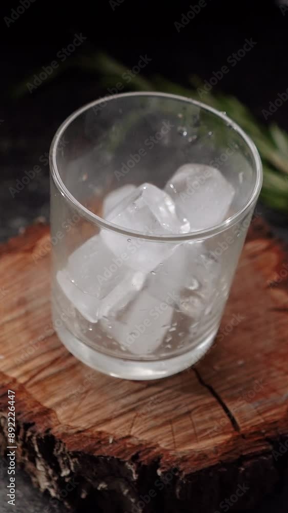 Ice cubes fall into a glass with lime and rosemary and topped with soda. The process of preparing a cocktail and a refreshing summer drink with alcohol for a party. Cold water with gin Ice cubes fall into a glass with lime and rosemary and topped with soda. The process of preparing a cocktail and a refreshing summer drink with alcohol for a party. Cold water with gin
