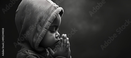 Black and white photo of an African American boy wearing hoodie, praying with hands folded in prayer isolated on black background