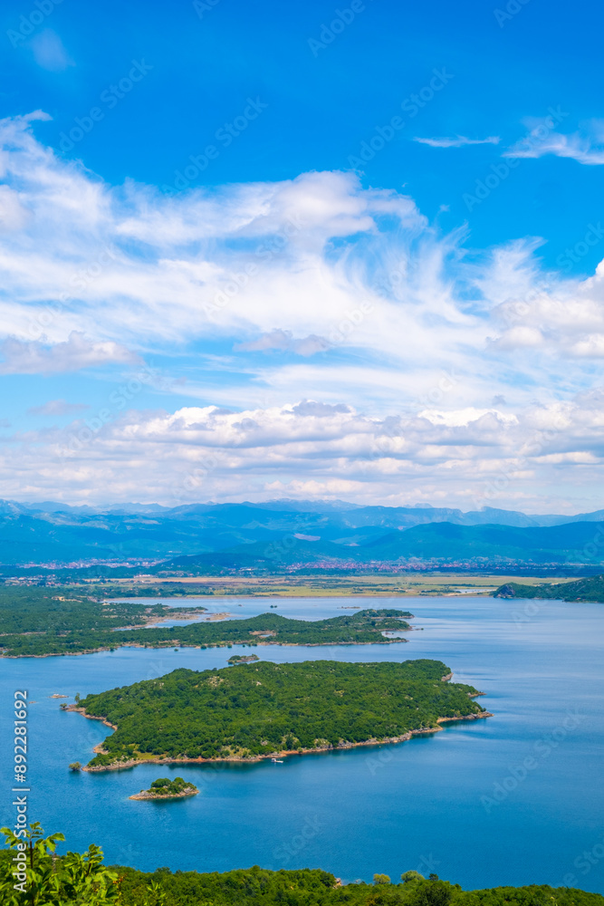A serene lake nestled amidst towering mountains, with several islands, all beneath a cloud-filled sky A serene lake nestled amidst towering mountains, with several islands, all beneath a cloud-filled sky