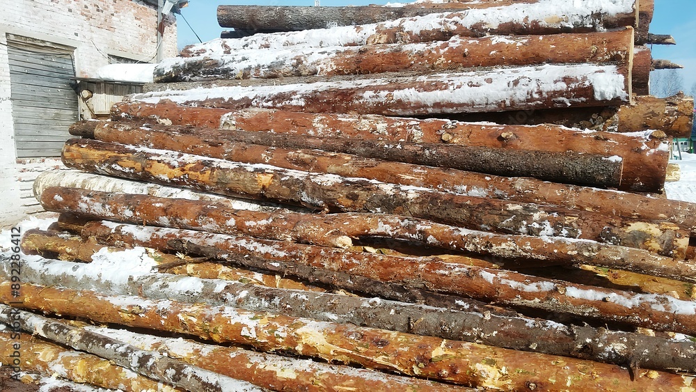 a large stack of cut logs piled up in an outdoor area. The logs are of varying lengths and are arranged in a crisscross pattern. They appear to be covered with patches of snow, indicating a cold a large stack of cut logs piled up in an outdoor area. The logs are of varying lengths and are arranged in a crisscross pattern. They appear to be covered with patches of snow, indicating a cold