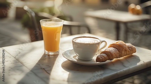 A cup of coffee, a glass of orange juice, and a croissant on a cafe table.