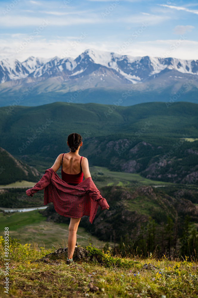 Naklejka premium girl in a red shirt looks at the peaks of snow-capped mountains