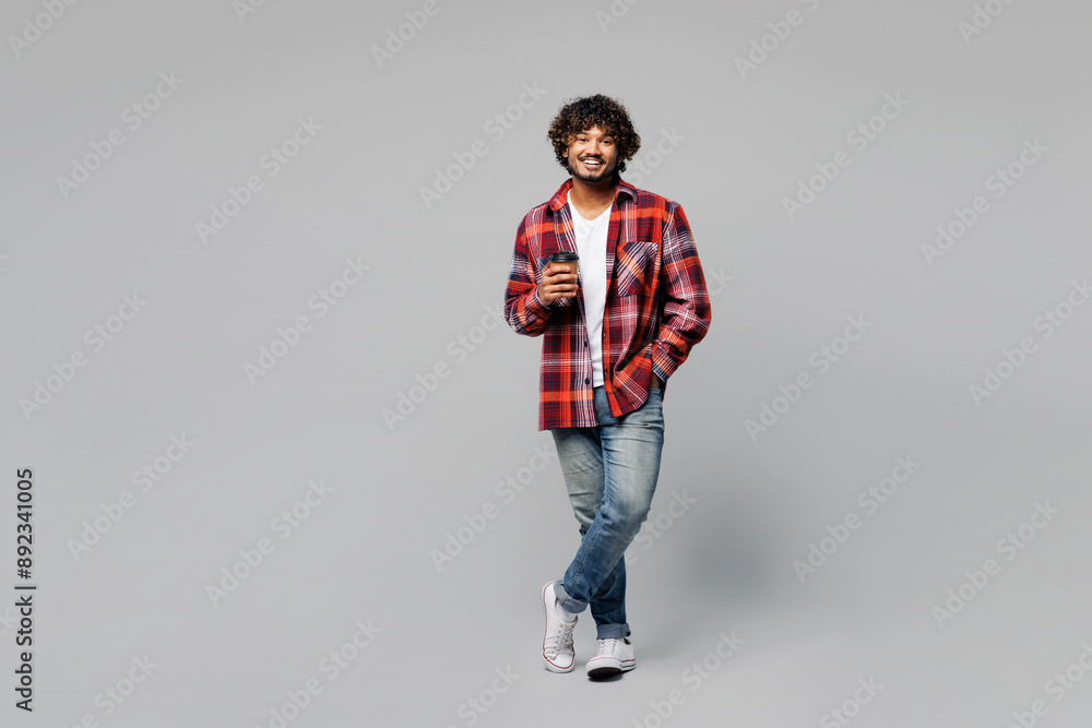 Young happy smiling Indian man he wears red shirt casual clothes hold takeaway delivery craft paper brown cup coffee to go isolated on plain grey color background studio portrait. Lifestyle concept. Young happy smiling Indian man he wears red shirt casual clothes hold takeaway delivery craft paper brown cup coffee to go isolated on plain grey color background studio portrait. Lifestyle concept.
