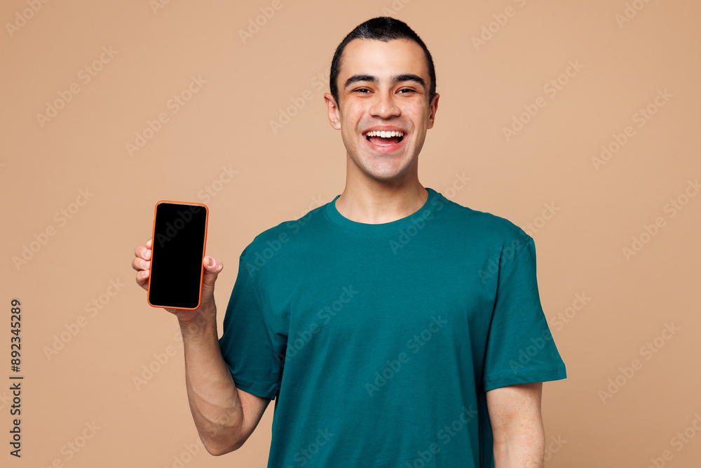 Young middle eastern man wear blue t-shirt casual clothes hold in hand use mobile cell phone with blank screen workspace area isolated on plain pastel light beige background studio. Lifestyle concept. Young middle eastern man wear blue t-shirt casual clothes hold in hand use mobile cell phone with blank screen workspace area isolated on plain pastel light beige background studio. Lifestyle concept.