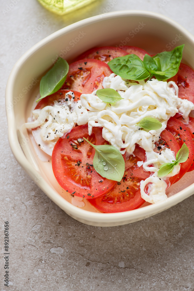 Beige serving tray with red tomato slices, stracciatella di bufala and basil, vertical shot, middle close-up, selective focus Beige serving tray with red tomato slices, stracciatella di bufala and basil, vertical shot, middle close-up, selective focus