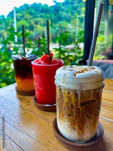 A selection of refreshing drinks including iced coffee, watermelon smoothie, and citrus iced tea on a wooden table, set against a lush tropical backdrop. Perfect for food and beverage themes.