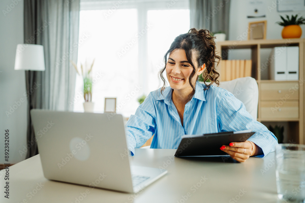 One young beautiful caucasian business woman working in office on laptop and looking through charts One young beautiful caucasian business woman working in office on laptop and looking through charts