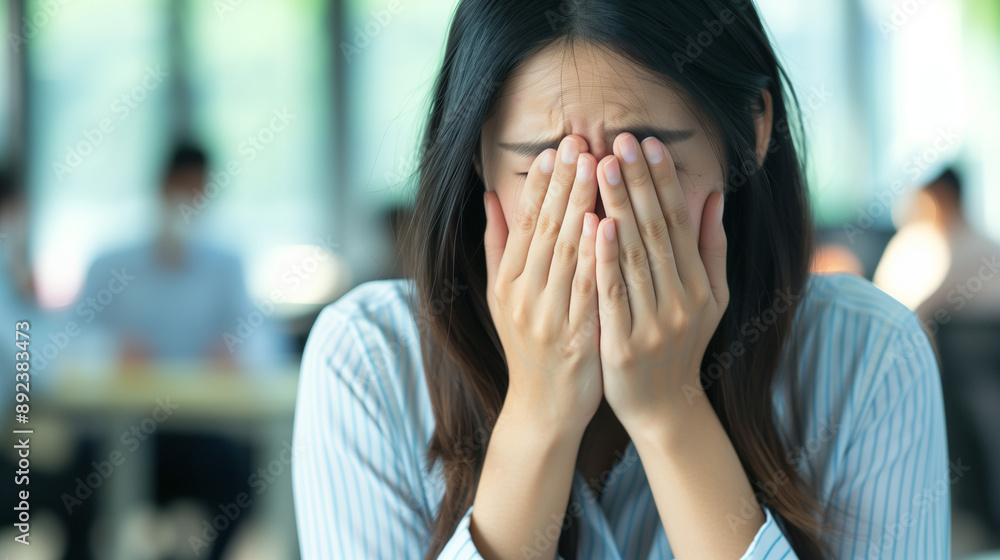 Distressed Asian businesswoman covering face with hands in office. Distressed Asian businesswoman covering face with hands in office.