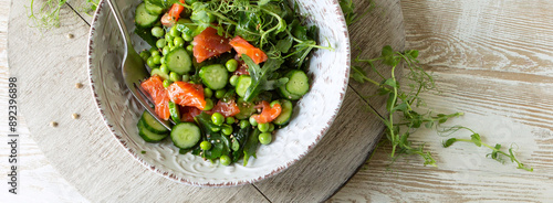 bowl of salad with red fish, cucumbers and green peas on the table