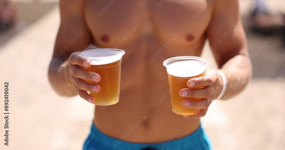 Hands hold two plastic glasses with beer on the beach in summer. Concept of cultural consumption of beer among tourists Hands hold two plastic glasses with beer on the beach in summer. Concept of cultural consumption of beer among tourists