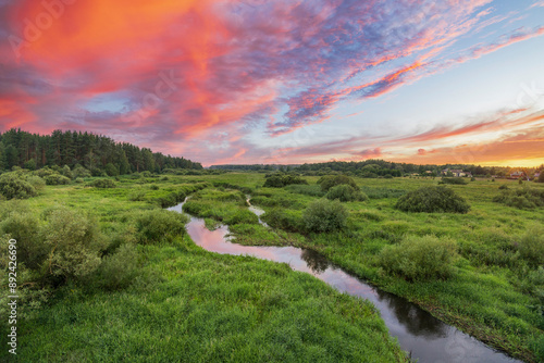 Photography A winding river flows through a verdant meadow, bathed in the golden light of a beautiful sunset
