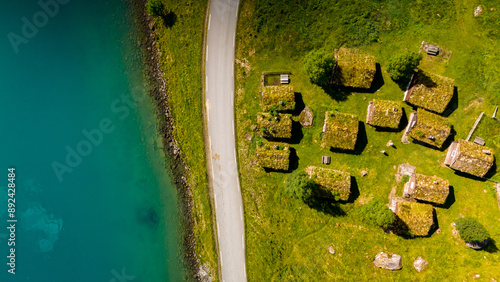 Aerial view of a small village in Norway with traditional grass-covered rooftops nestled amongst green fields and a winding road leading to a sparkling lake. lovatnet lake Lodal valley Norway photo