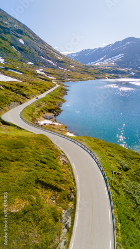 An aerial view of a winding road snaking through green mountains and a glistening blue lake in Norway. Langvatnet, Geiranger, Norway photo