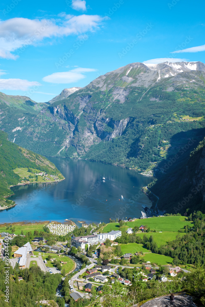 A breathtaking view of the Geirangerfjord in Norway, with towering mountains and a sparkling blue water, revealing a charming village at the foot of the fjord. A breathtaking view of the Geirangerfjord in Norway, with towering mountains and a sparkling blue water, revealing a charming village at the foot of the fjord.
