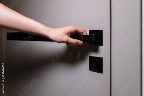 An unrecognizable woman reaches out with her hand to a modern door and a black door handle to open the room photo