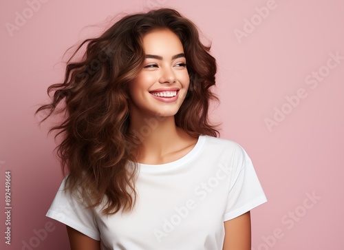 Portrait of a smiling beautiful woman in a white t-shirt looking away over a pink background with copy space, side view