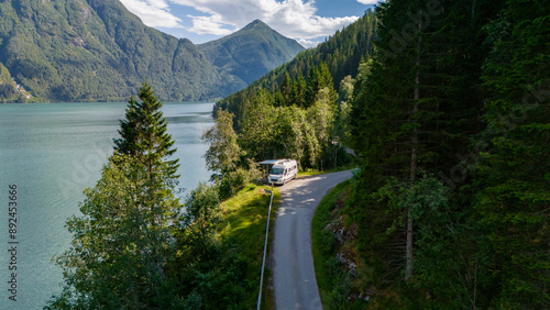 A white campervan parks on a winding road overlooking a picturesque Norwegian fjord, surrounded by lush green forests and mountains. Fjaerlandsfjorden, Fjord, Vestland, Norway photo