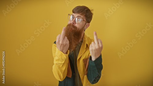 Handsome redhead bearded man in glasses showing middle fingers against a vibrant yellow background, projecting attitude.