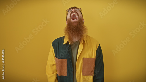 Bearded redhead man shouting and looking up against an isolated yellow background.