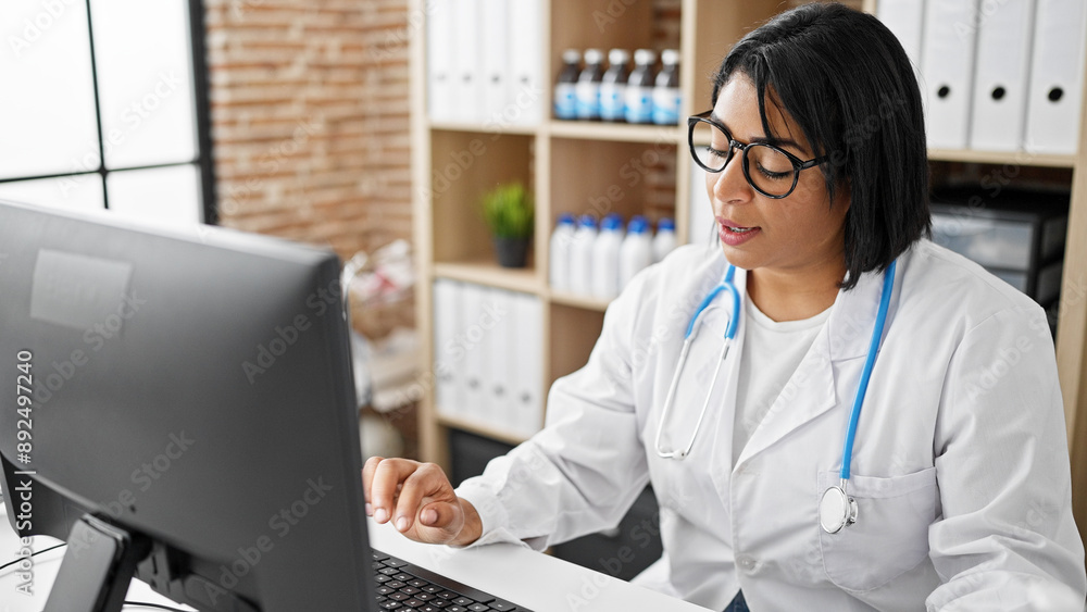A hispanic woman healthcare professional works diligently on a computer in a clinic office setting, symbolizing modern medical practice. A hispanic woman healthcare professional works diligently on a computer in a clinic office setting, symbolizing modern medical practice.