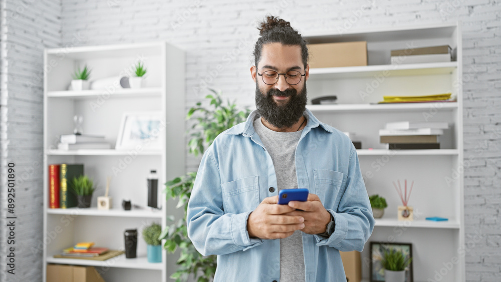 A bearded young man smiling at his phone in a modern office, exuding casual professionalism. A bearded young man smiling at his phone in a modern office, exuding casual professionalism.