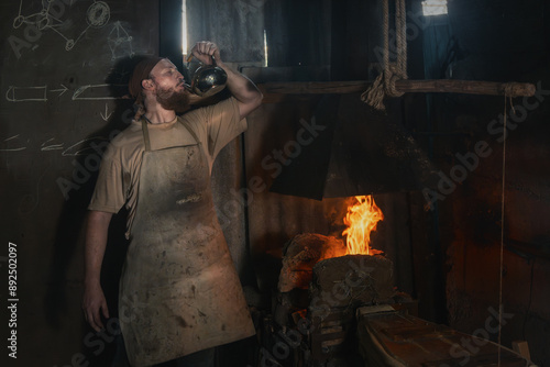 Wallpaper Mural Tired blacksmith drinks water from a metal kettle near a flame of fire in an old rural forge. Torontodigital.ca