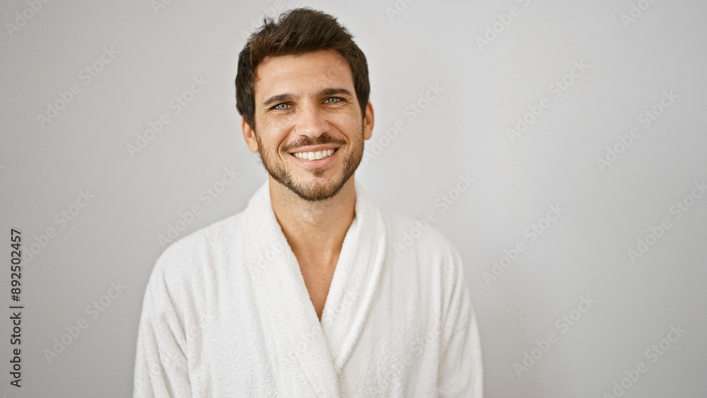 Handsome hispanic man with a beard smiling in a white bathrobe against an isolated white wall. Handsome hispanic man with a beard smiling in a white bathrobe against an isolated white wall.