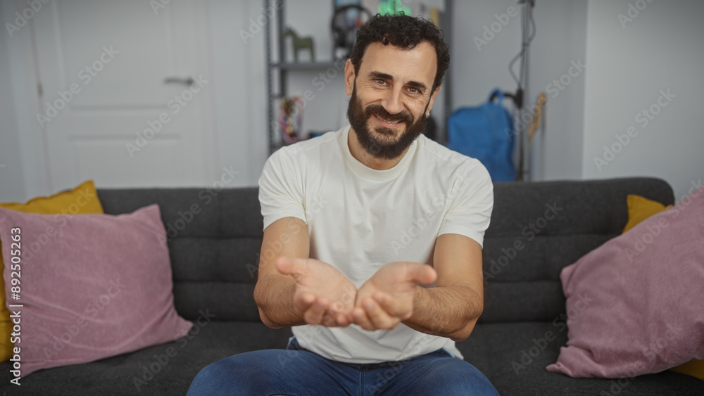 Middle-aged man with beard smiling, extending hands in a cozy living room setting Middle-aged man with beard smiling, extending hands in a cozy living room setting