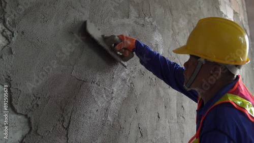 Asian construction worker carefully plastering a wall with cement at the construction site of an unfinished house.