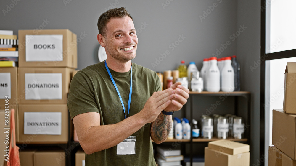 A cheerful young man applauding in a storeroom with labeled boxes and donations. A cheerful young man applauding in a storeroom with labeled boxes and donations.