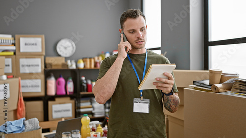 Fényképezés Handsome man with beard talking on phone and holding notebook in warehouse