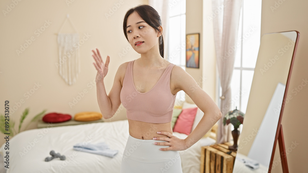 Obraz premium A young asian woman strikes a casual pose in her stylish bedroom with natural light and contemporary decor.